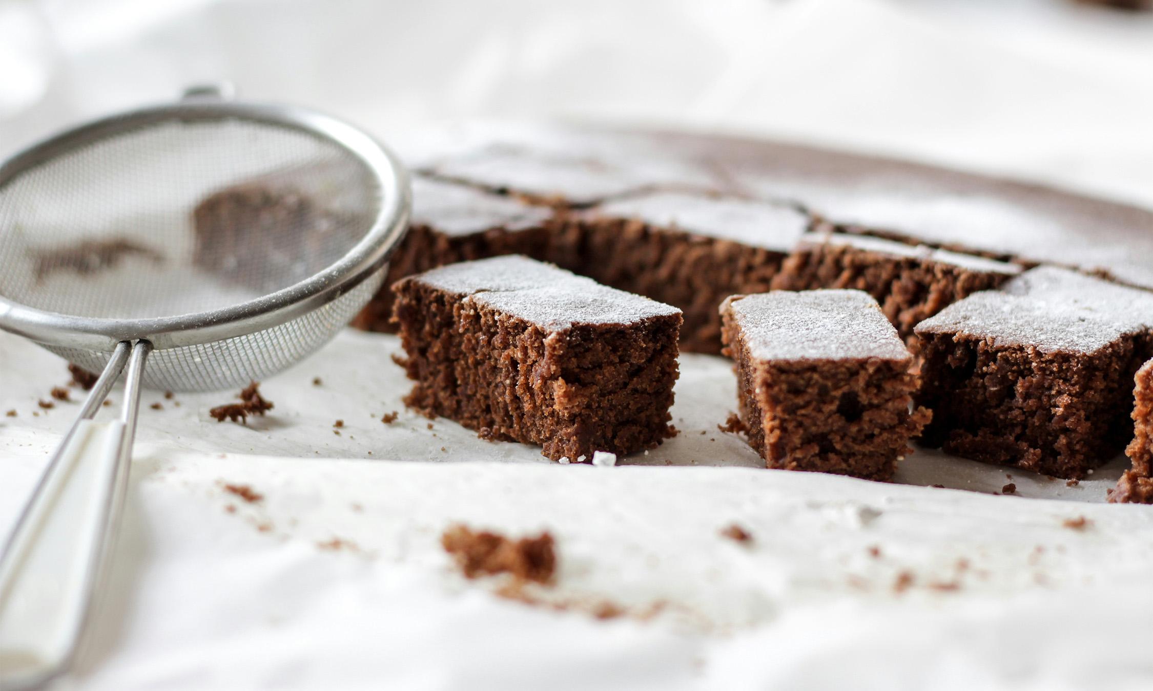 Some brownies on a white towel next to a small sifter for powdered sugar.