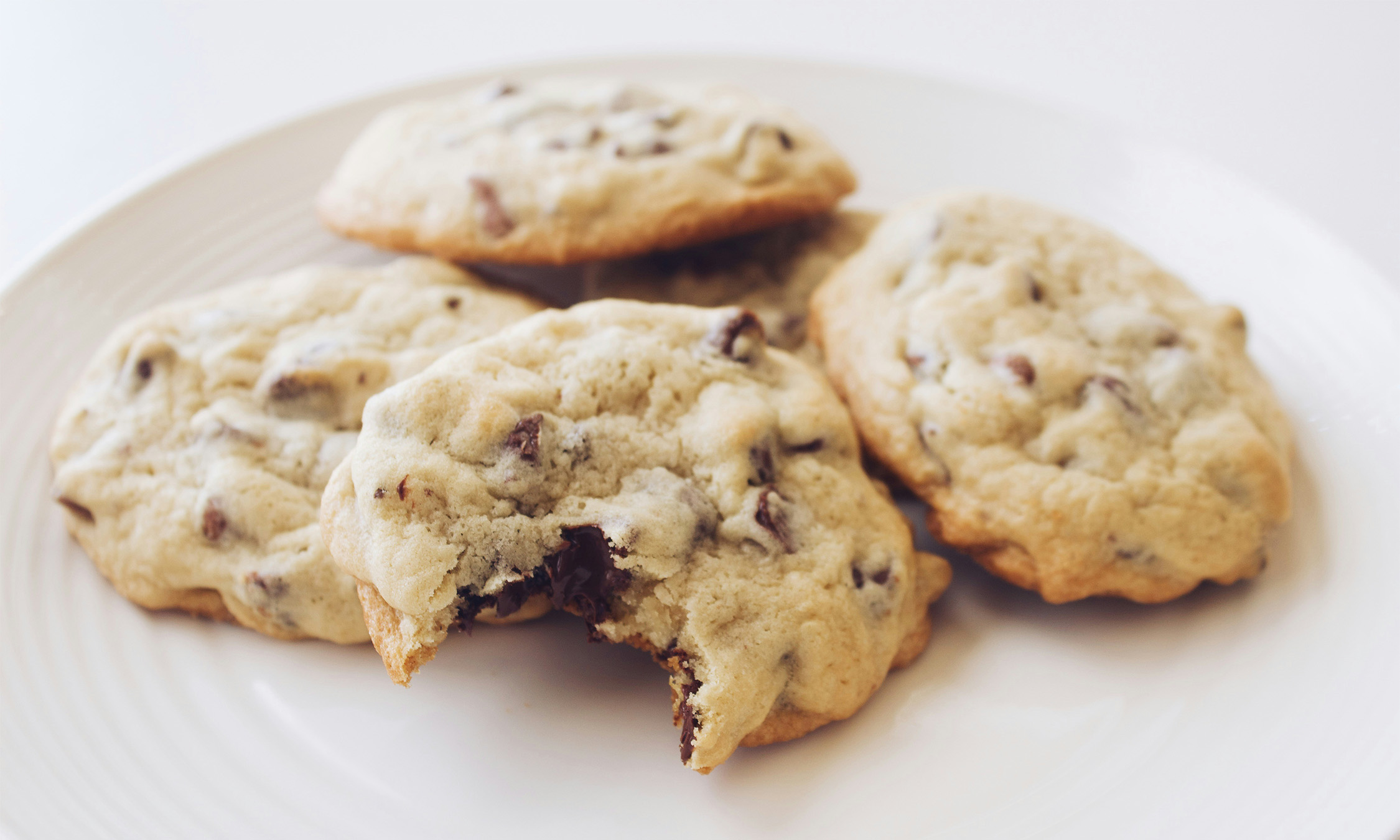 A white plate with a pile of cookies with a bite taken out of one of them.