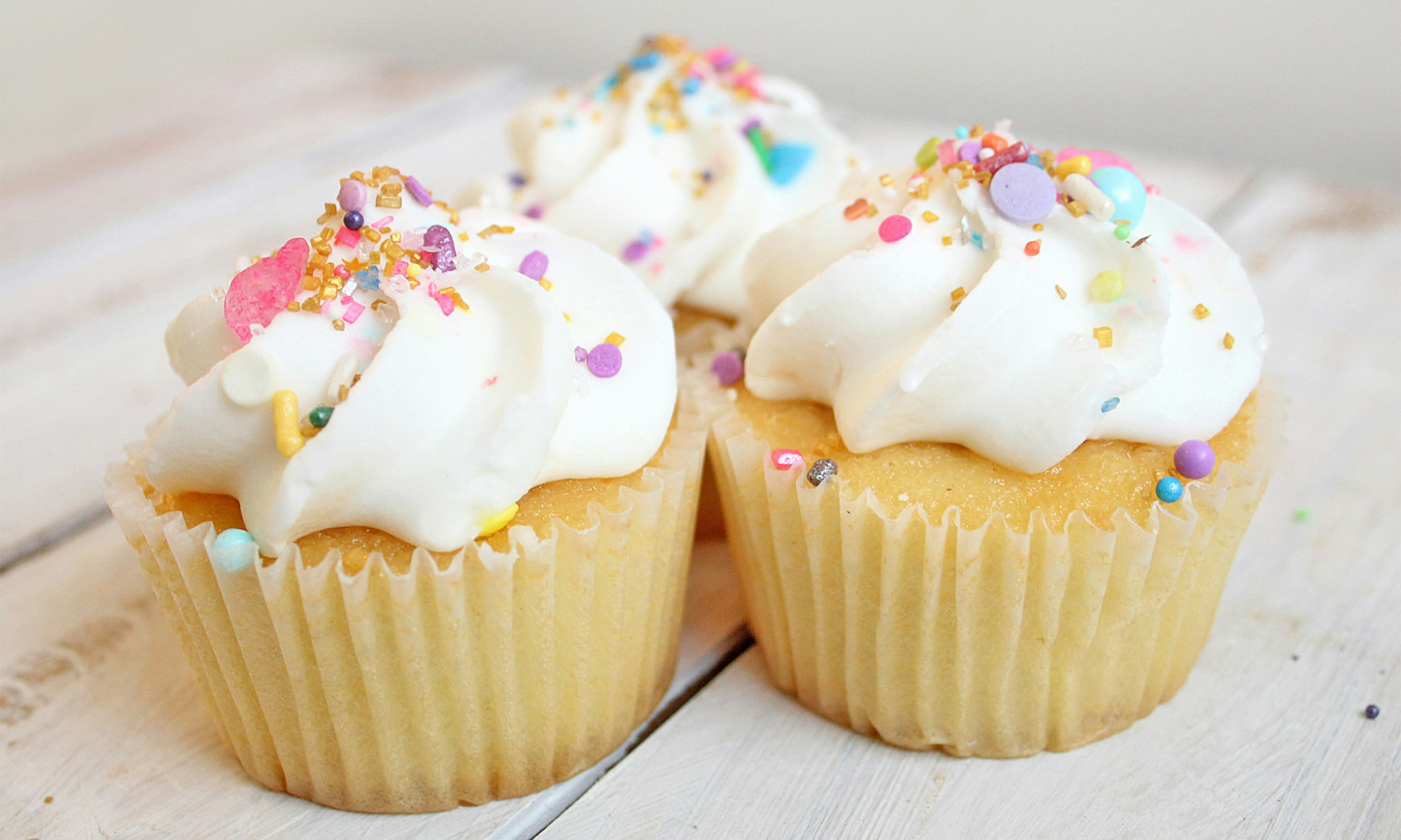 Three vanilla cupcakes with white frosting and sprinkles.