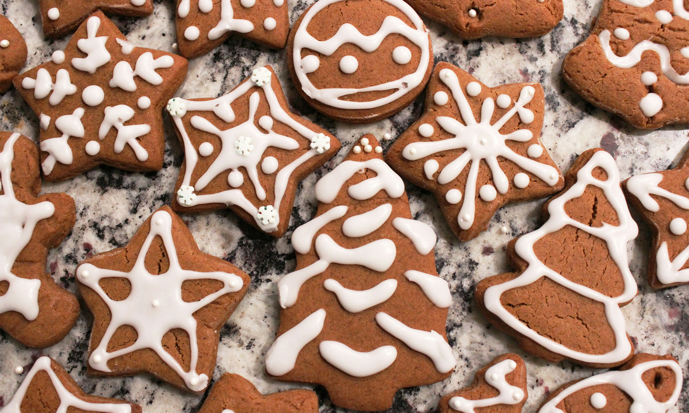 Gingerbread cookies shaped as stars and trees layed out on a surface and decorated with white frosting.