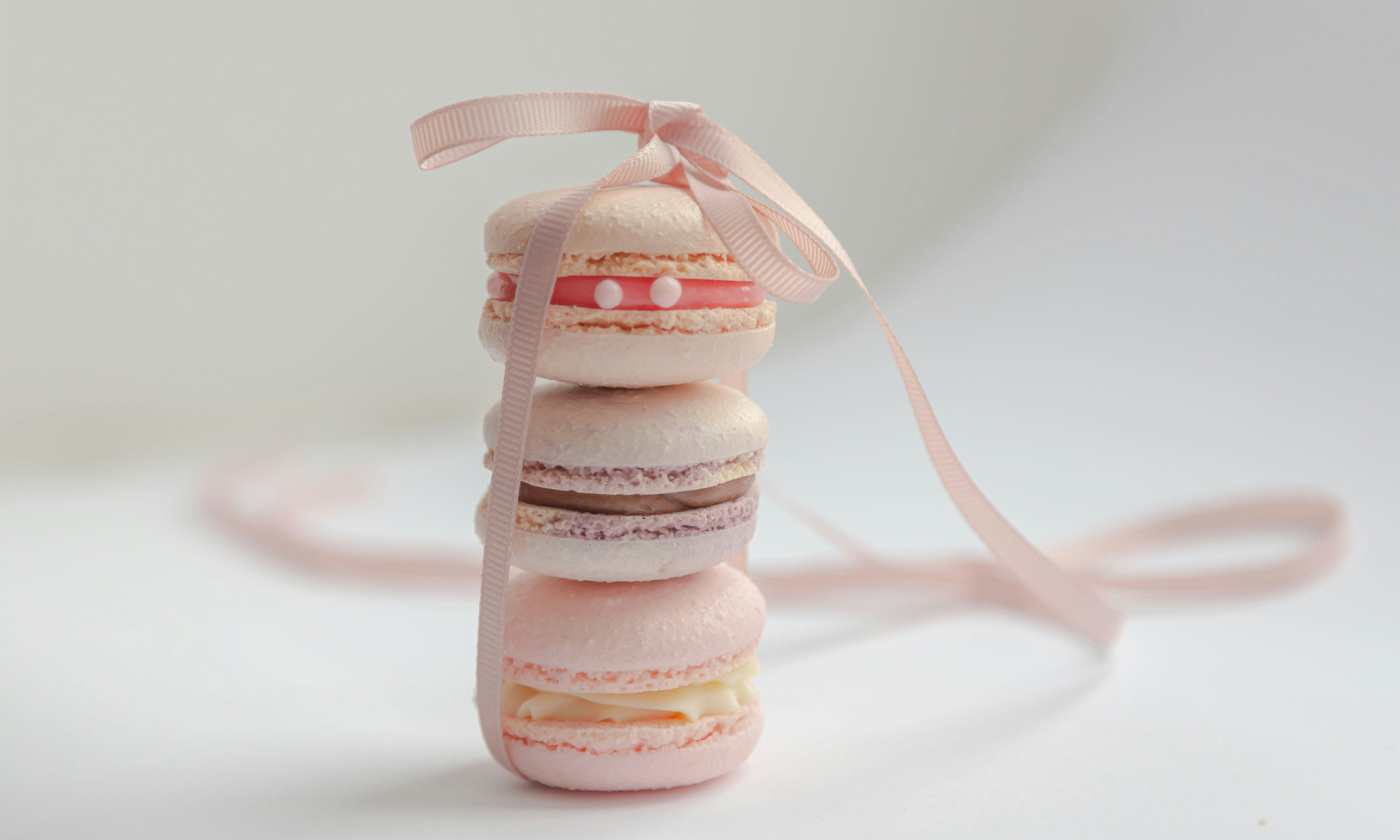 Three pink macarons stacked on top of each other and tied together with a pink ribbon.