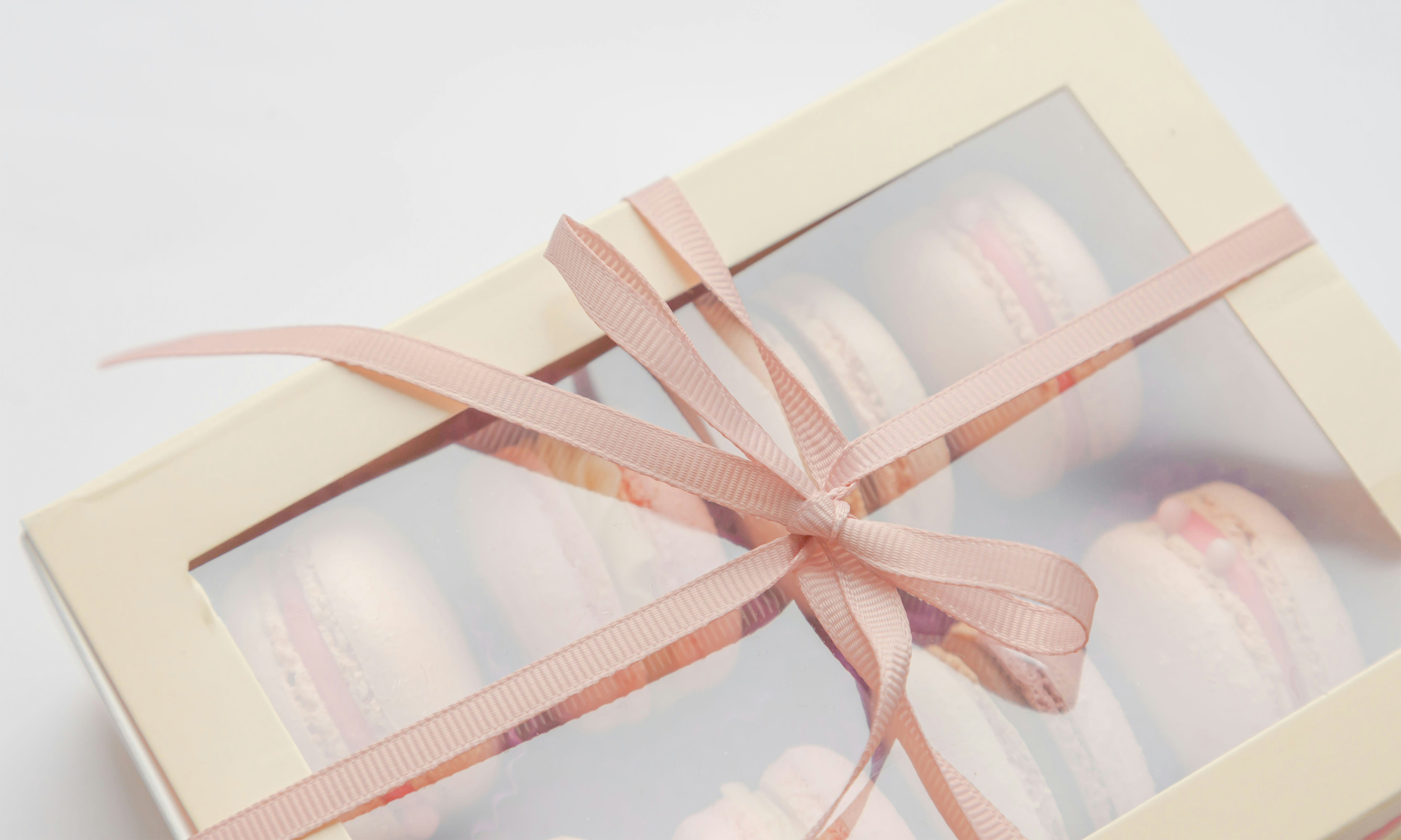 A white box with a clear top filled with macarons and tied together with pink ribbon.